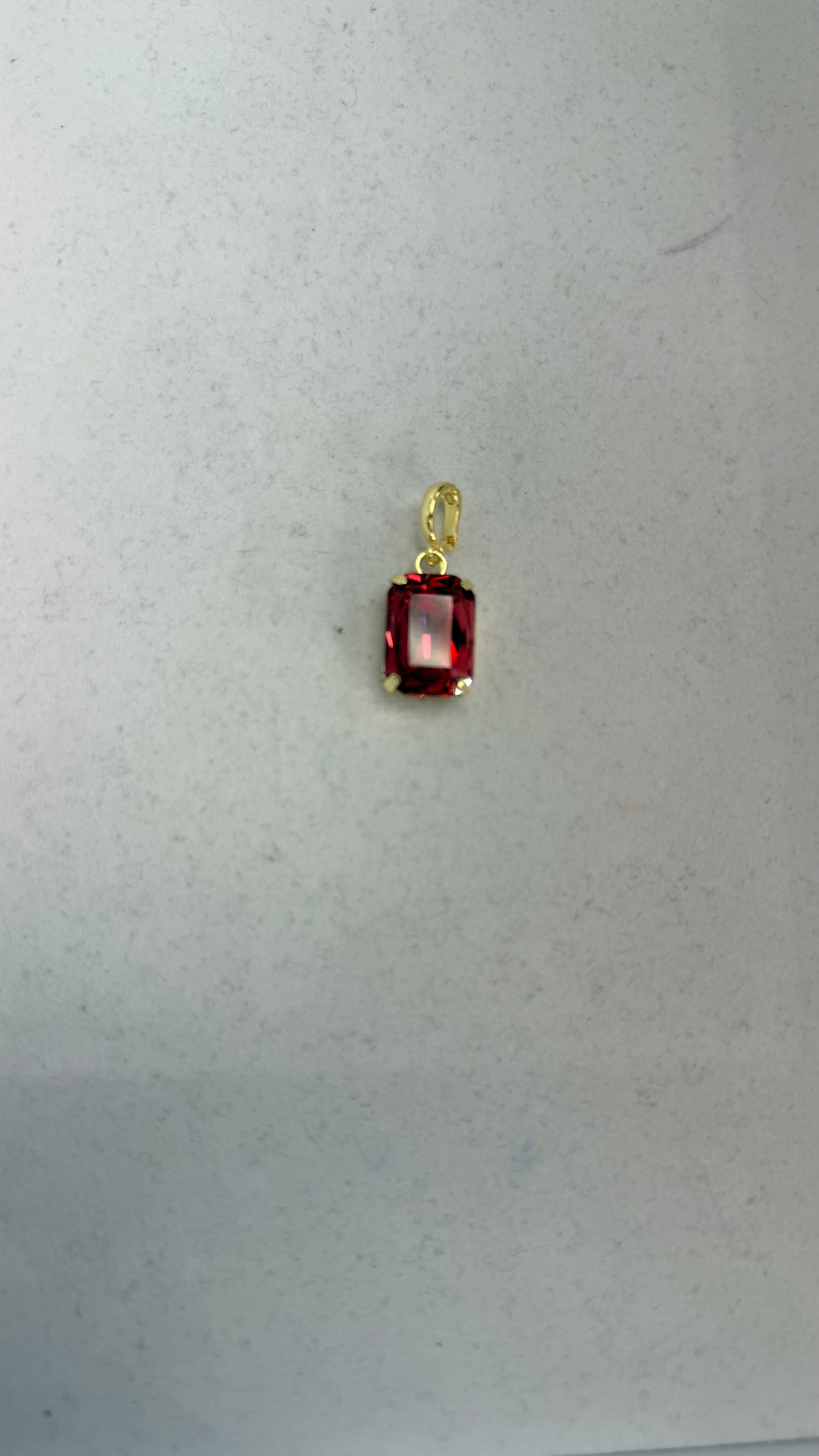 Small rectangular crimson red faceted gemstone pendant charm in a gold four-prong setting with oval bail.