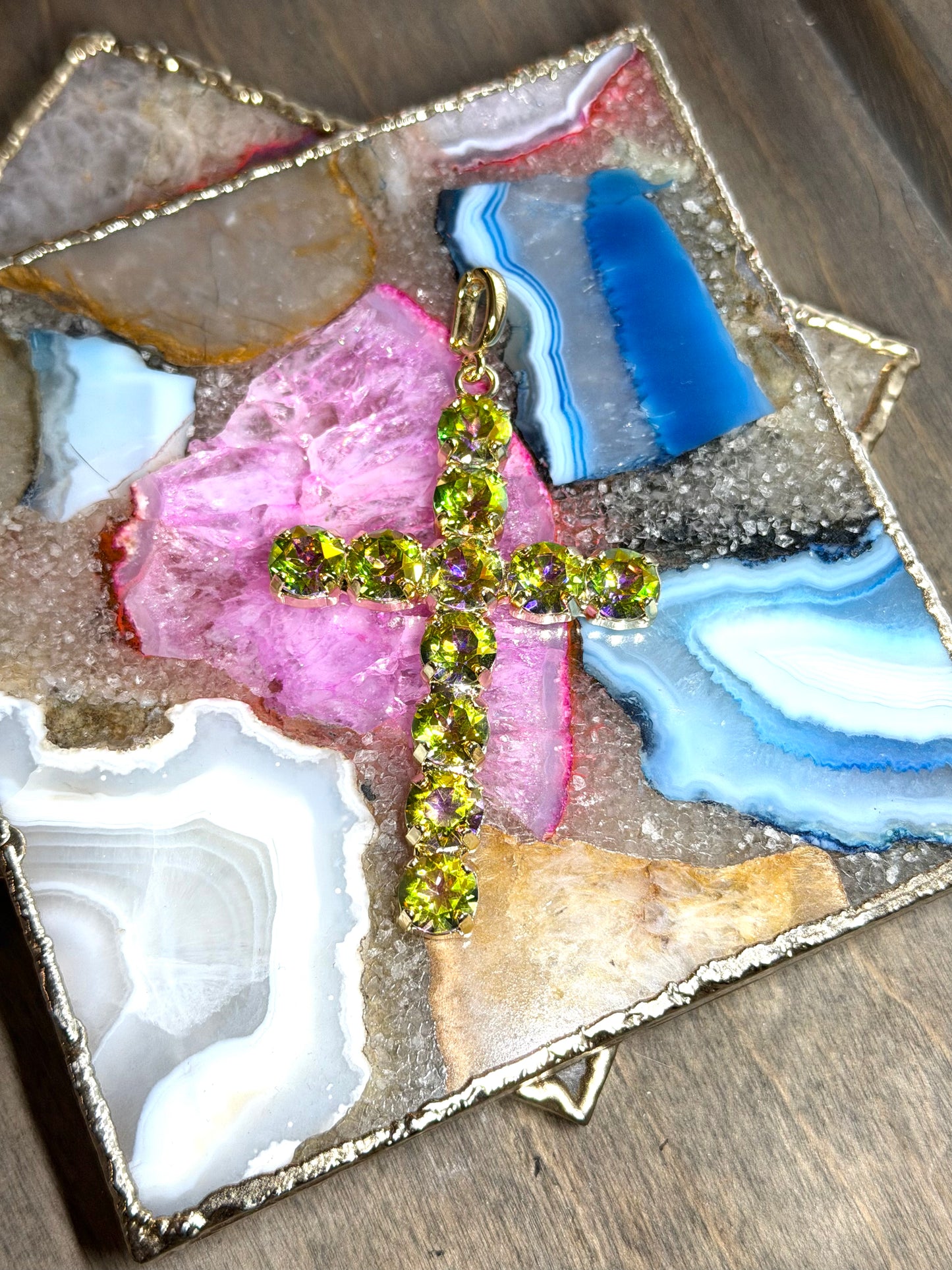 Large gold cross charm pendant with round peridot green faceted stones, displayed on a multicolor agate tray.