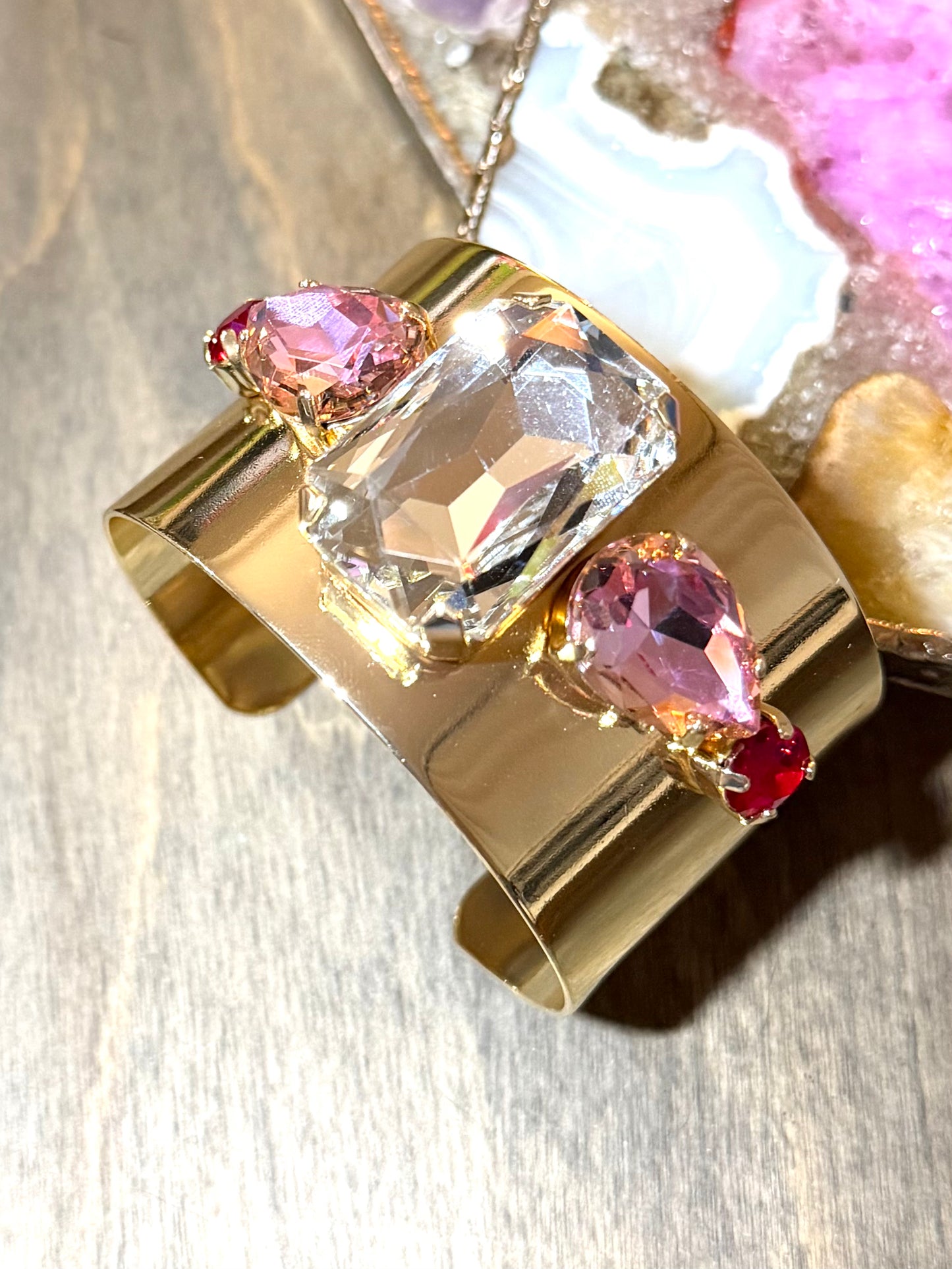 Wide gold cuff bracelet with large clear crystal center, pink pear-shaped stones, and ruby accents by AF Designs