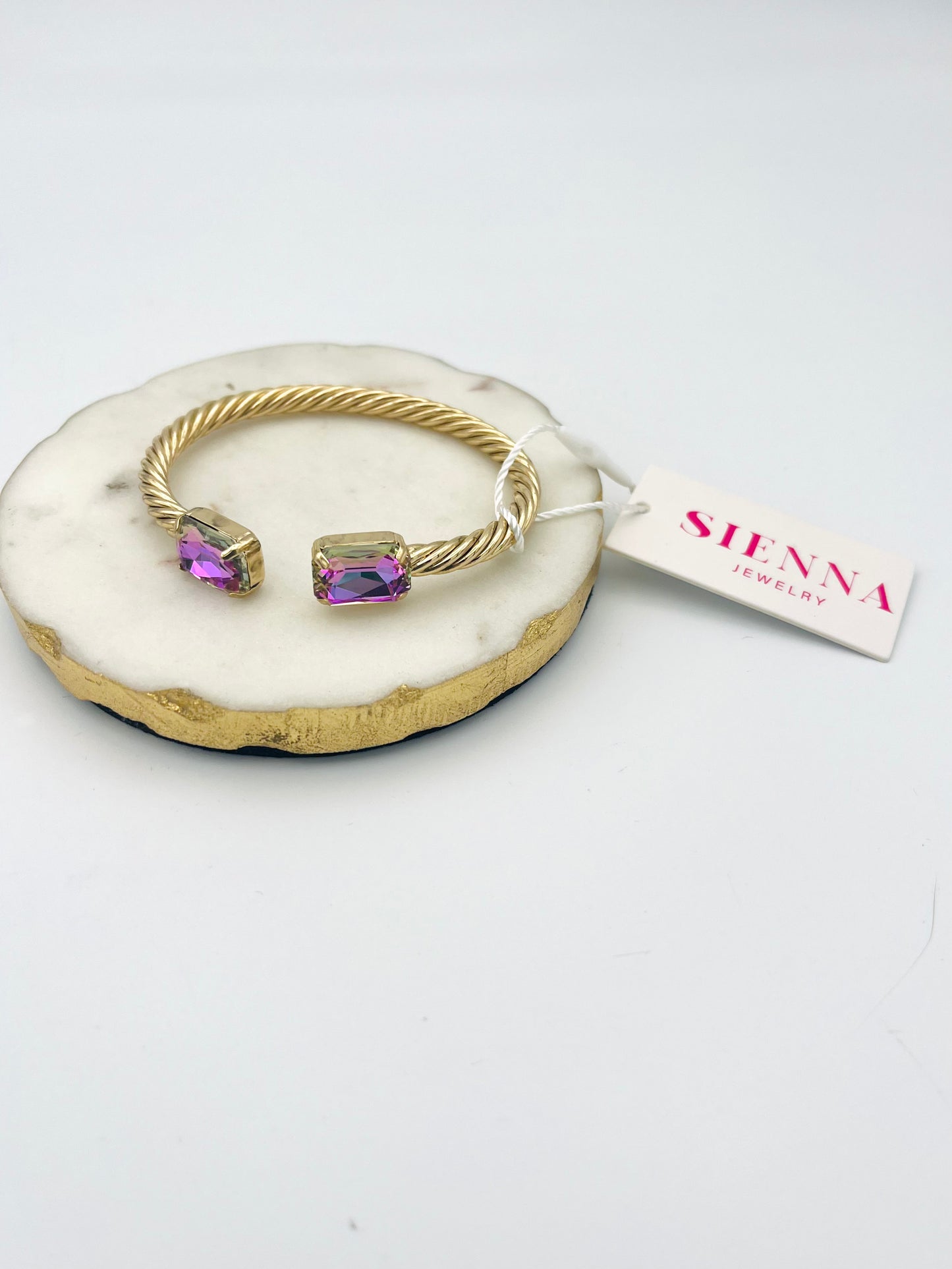 Gold twisted cable cuff bracelet with rectangular pink-purple gemstones on white agate display