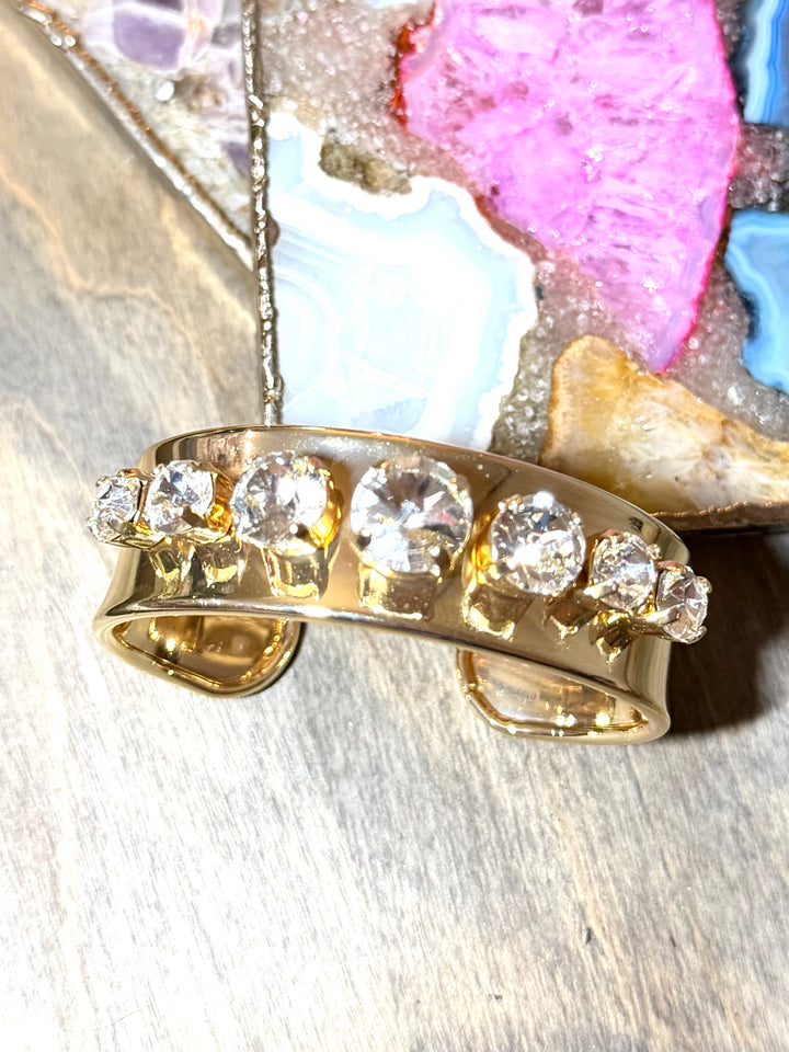 Gold cuff bracelet with five round clear crystal stones in prong settings, wide polished band, open-back design