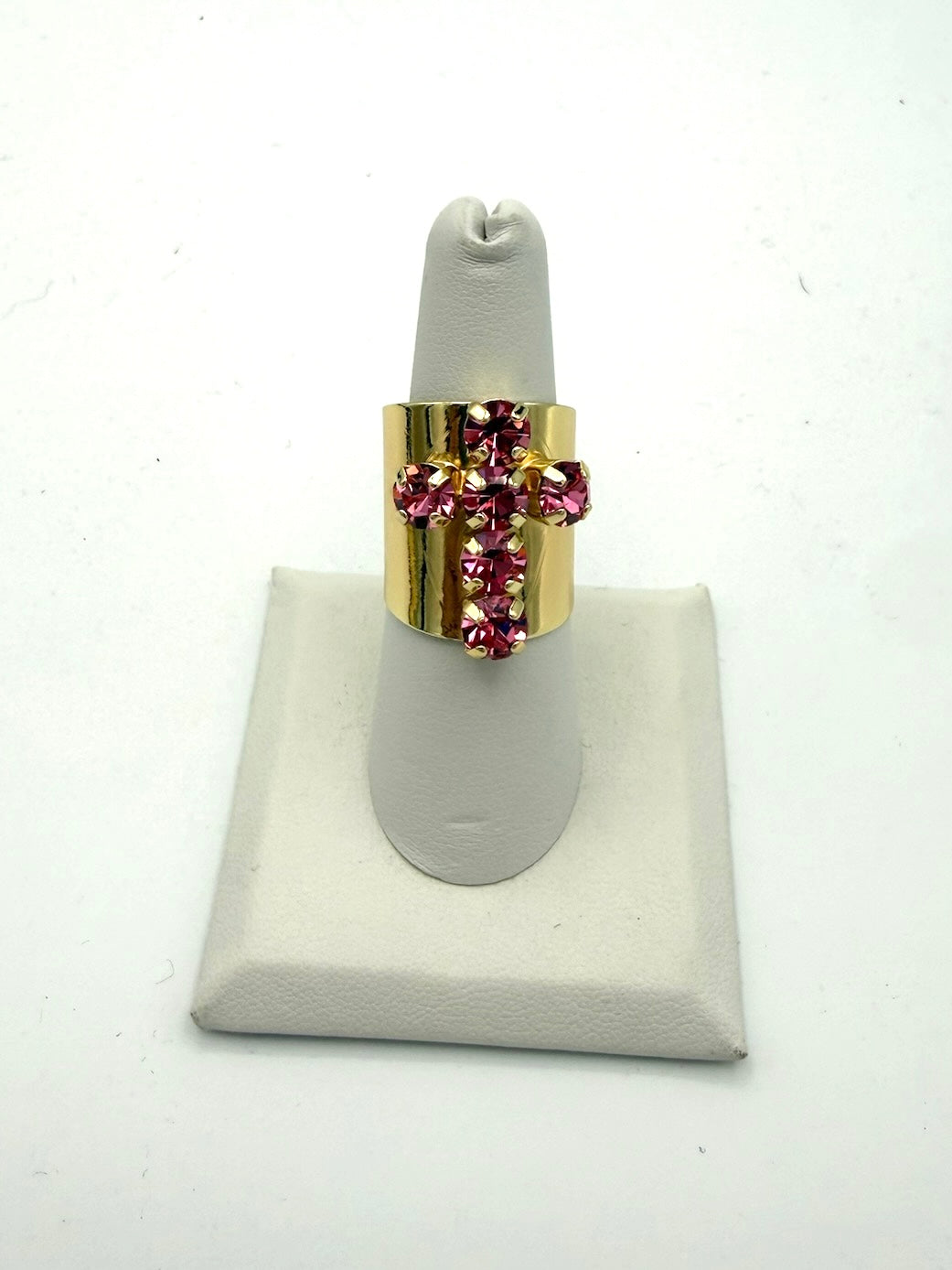 Wide gold band ring with hot pink rhinestone cross centerpiece on white display stand