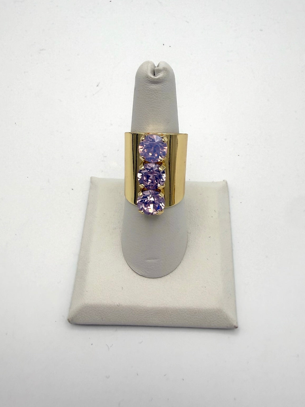 Triple Threat Ring in Lilac: wide gold band with three vertical round-cut lavender gemstones in prong settings.