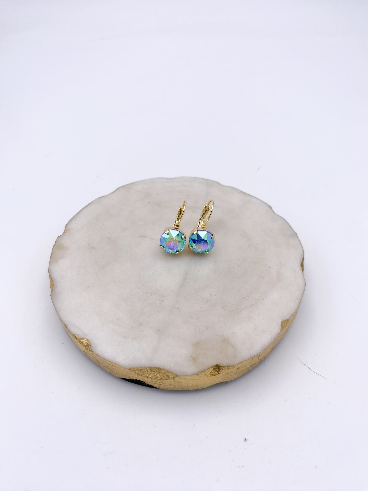 Gold lever-back drop earrings with iridescent aqua-teal-lavender faceted crystal stones on marble tray