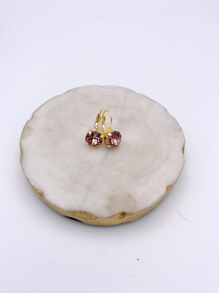 Gold lever-back drop earrings with round faceted blush pink peony crystals on white marble dish