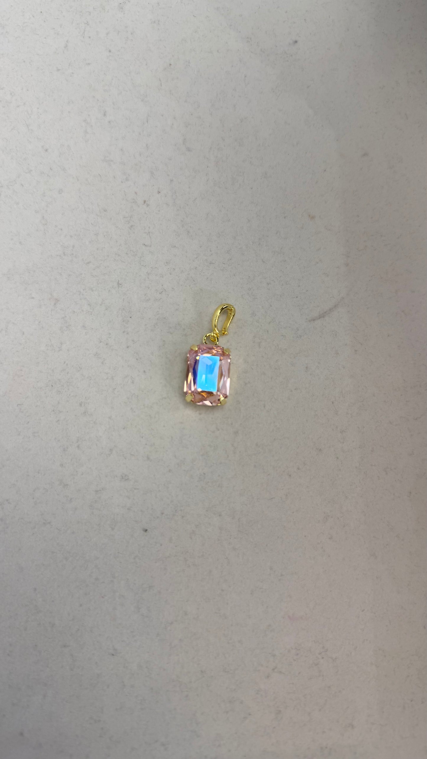 Small blush pink emerald-cut crystal charm pendant with gold prong setting and iridescent blue reflection