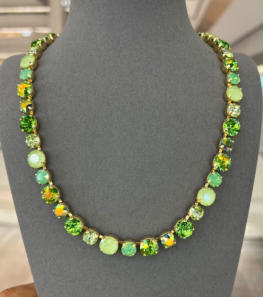 Green crystal tennis necklace with round stones in gold settings displayed on gray jewelry bust