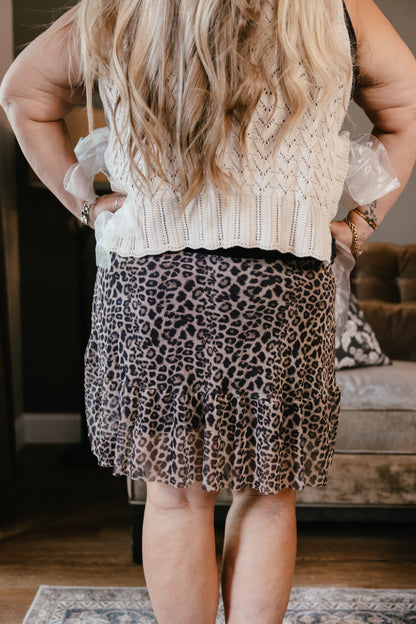 Leopard print mini skirt with ruffle hem paired with cream cable knit sweater vest