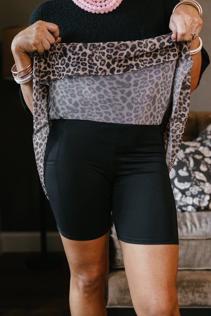 Black biker shorts with leopard print mesh skirt overlay featuring long tie straps, modeled by woman with silver jewelry