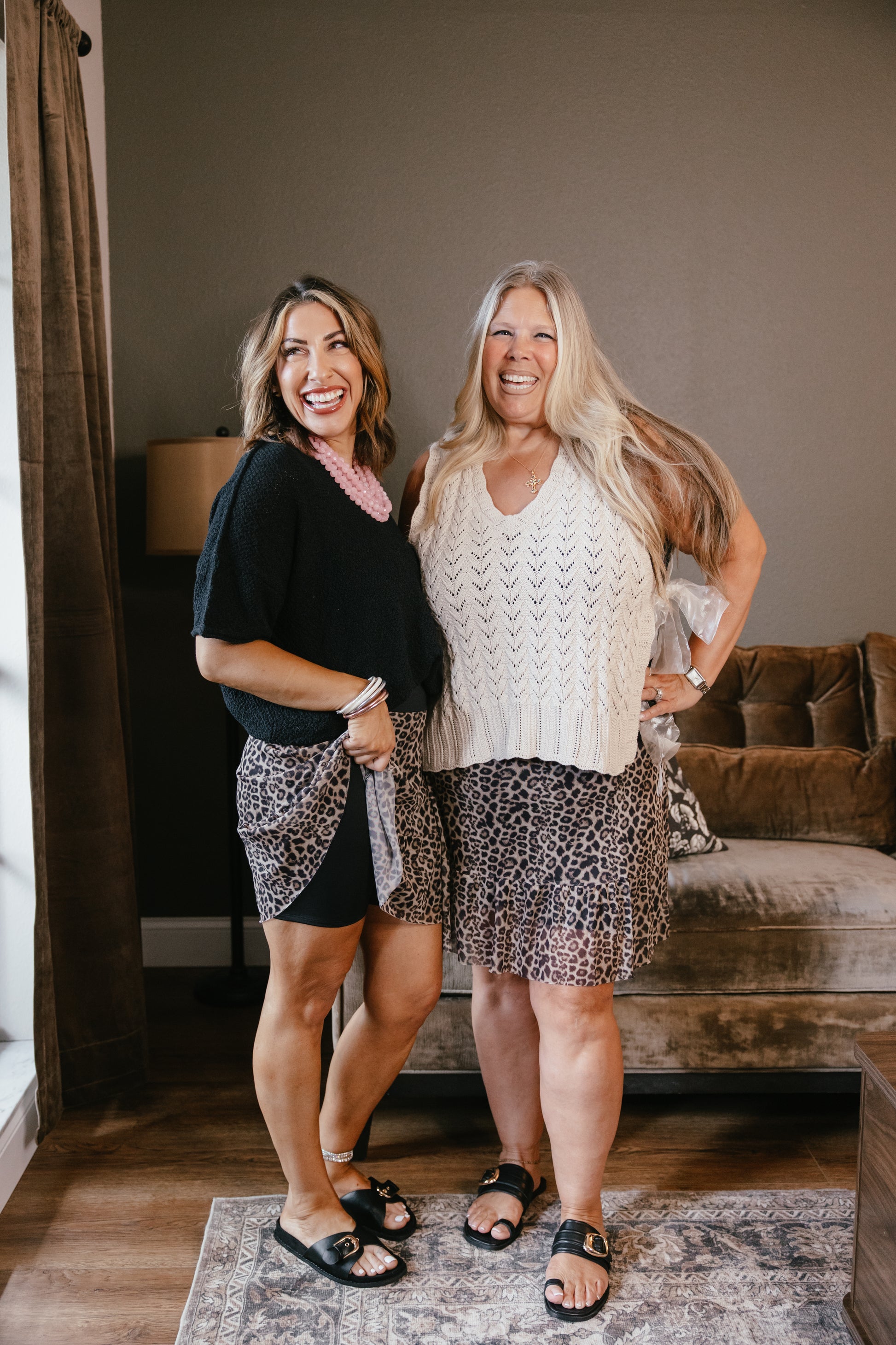 Two women modeling leopard print skirts with lace overlay, one in black top, one in cream sweater vest