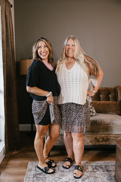 Two women modeling leopard print skirts with lace overlay, one in black top, one in cream sweater vest