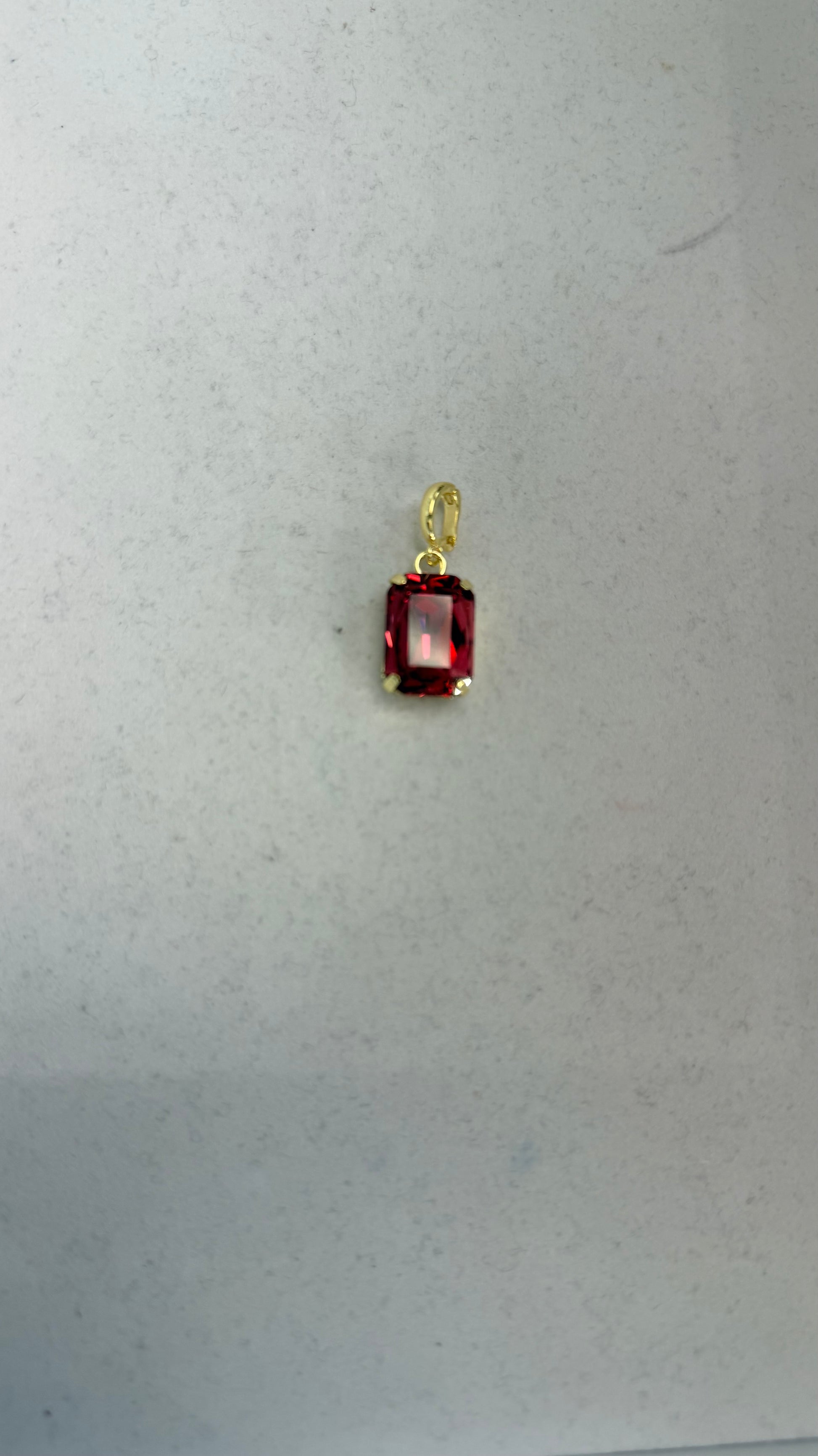 Small rectangular crimson red faceted gemstone pendant charm in a gold four-prong setting with oval bail.