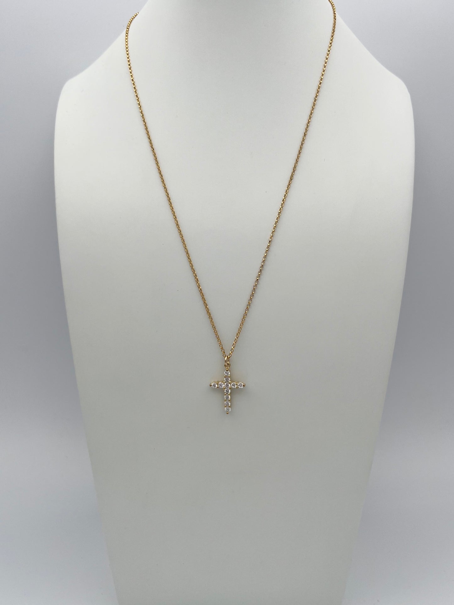 Gold chain necklace with crystal cross pendant displayed on white jewelry bust