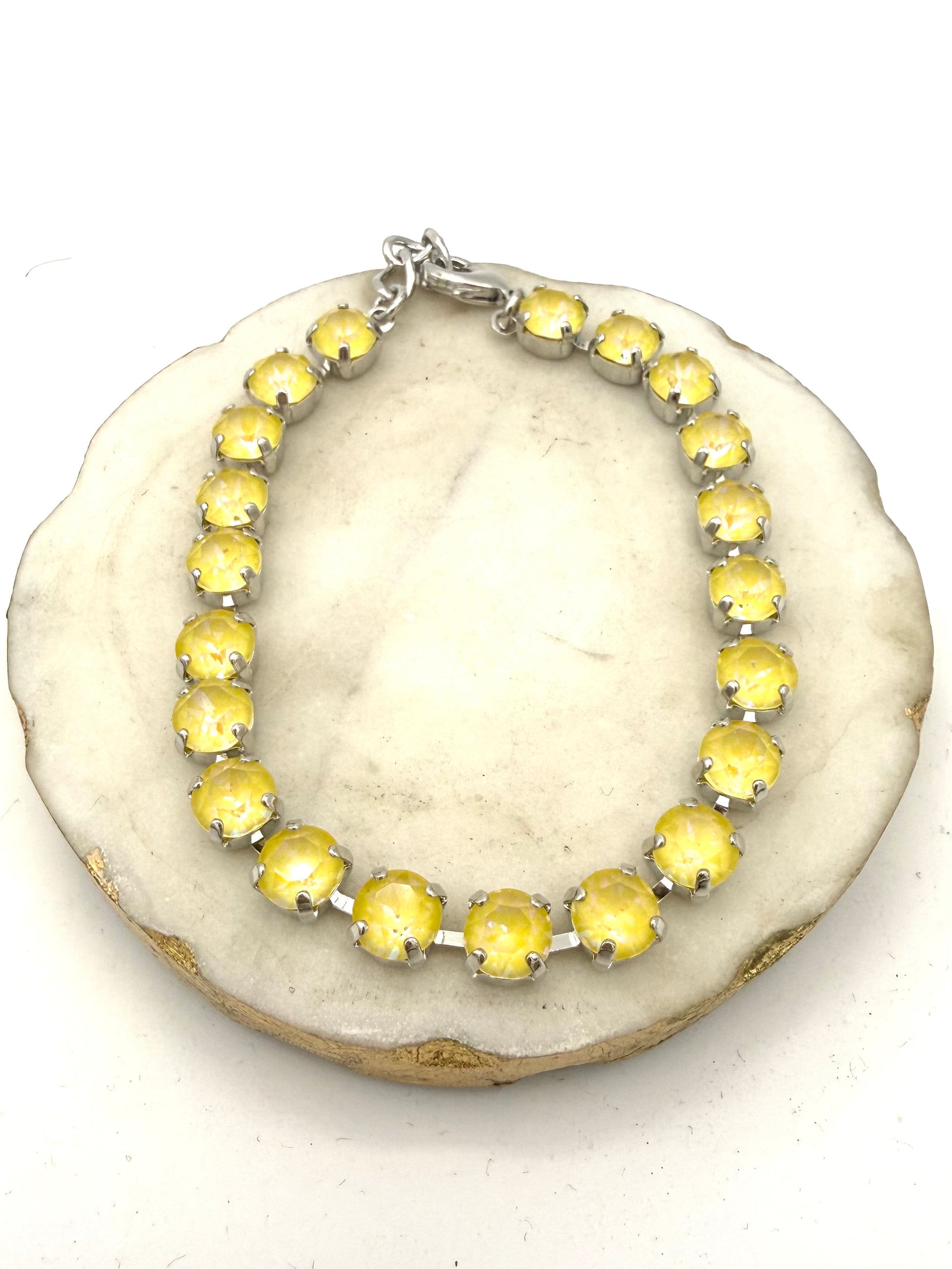 Silver tennis anklet with round milky yellow opalescent stones in prong settings with lobster clasp closure.