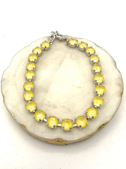 Silver tennis anklet with round milky yellow opalescent stones in prong settings with lobster clasp closure.