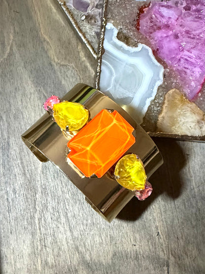 Wide gold cuff bracelet with neon orange center stone, yellow teardrop gems, and pink accents by AF Designs