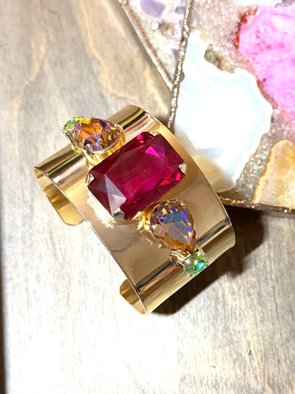 Wide gold cuff bracelet with large magenta crystal center and iridescent aurora borealis teardrop accents