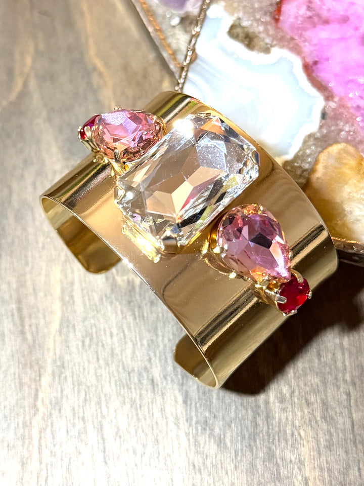 Wide gold cuff bracelet with large clear crystal center, pink pear-shaped stones, and ruby accents by AF Designs
