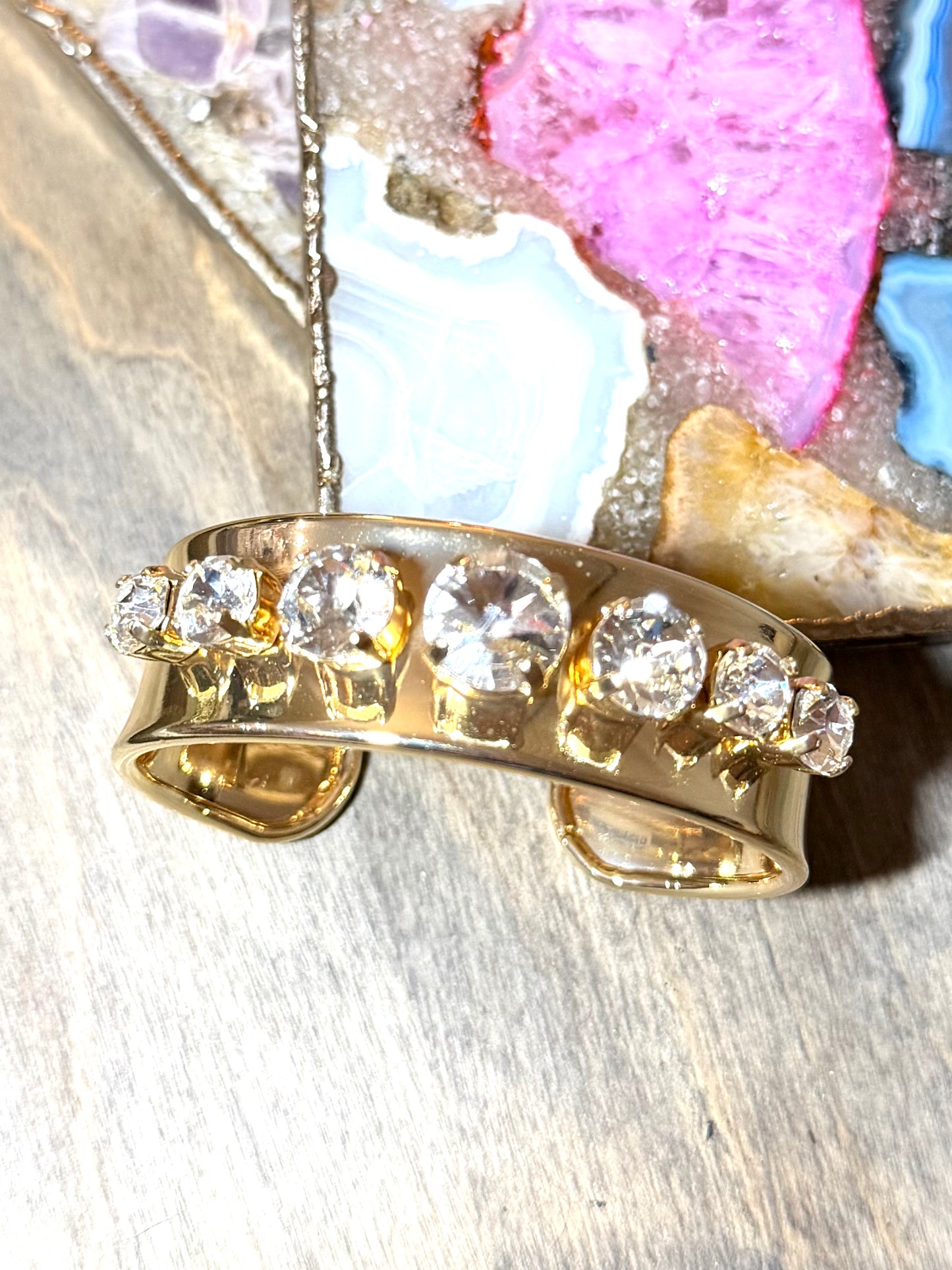 Gold cuff bracelet with five round clear crystal stones in prong settings, wide polished band, open-back design