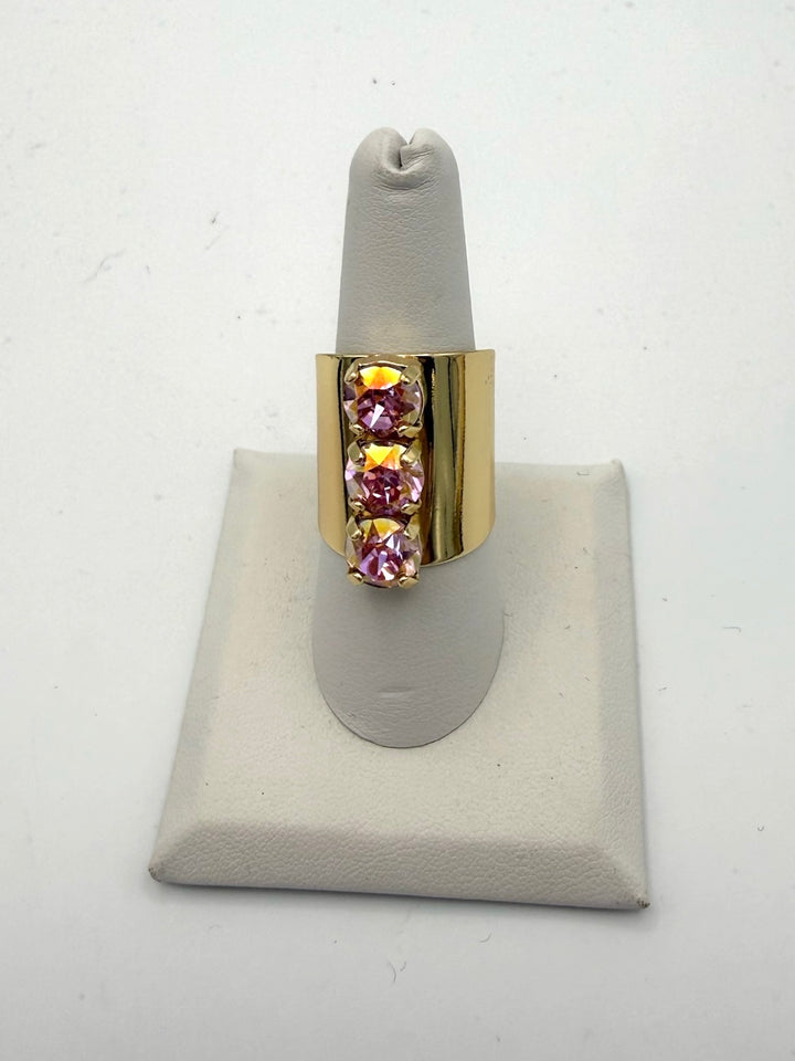 Wide gold-tone band ring with three vertical iridescent pink crystals in prong settings, statement cocktail style.