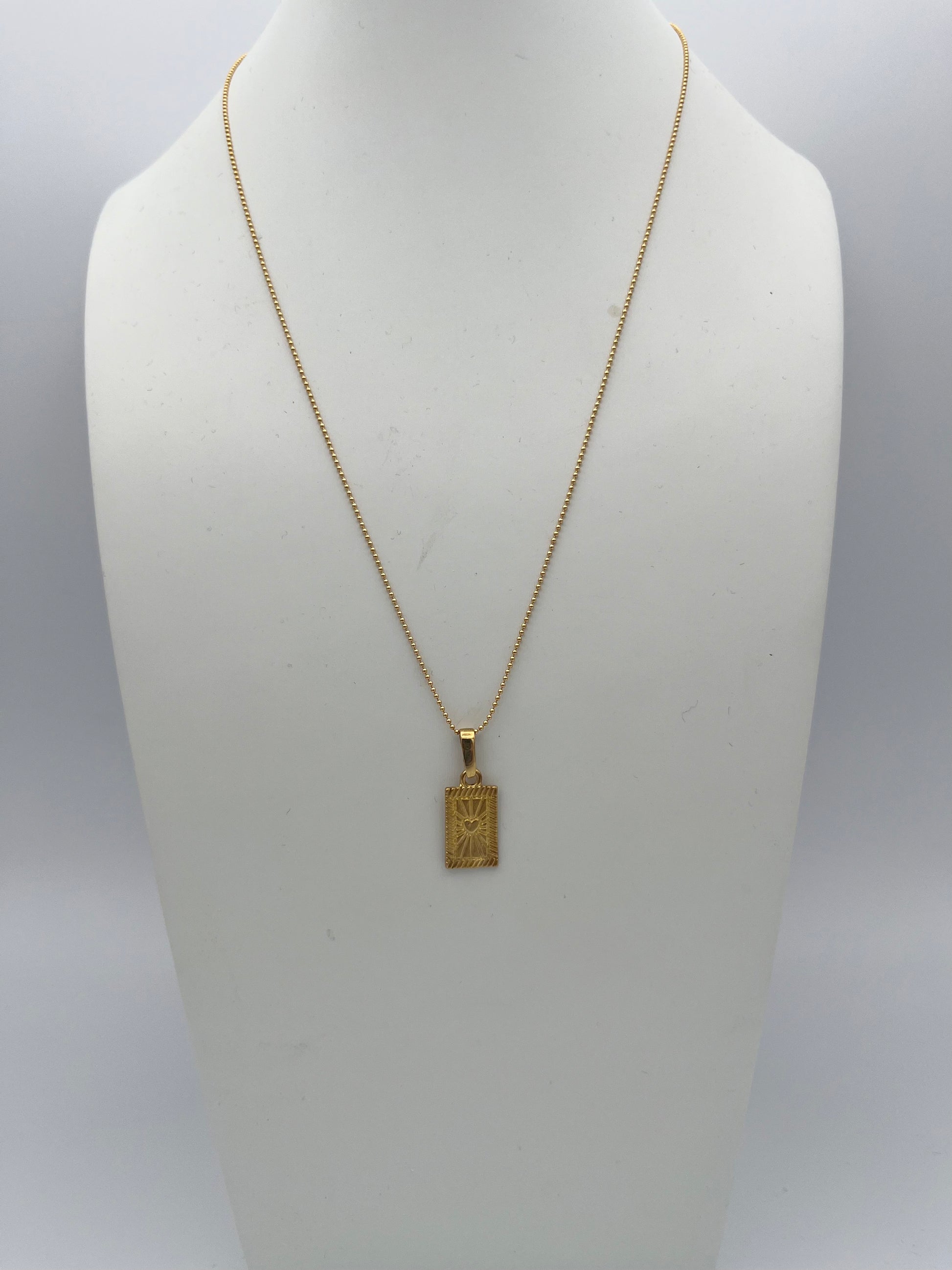 Gold chain necklace with rectangular pendant featuring engraved celestial design displayed on white jewelry bust