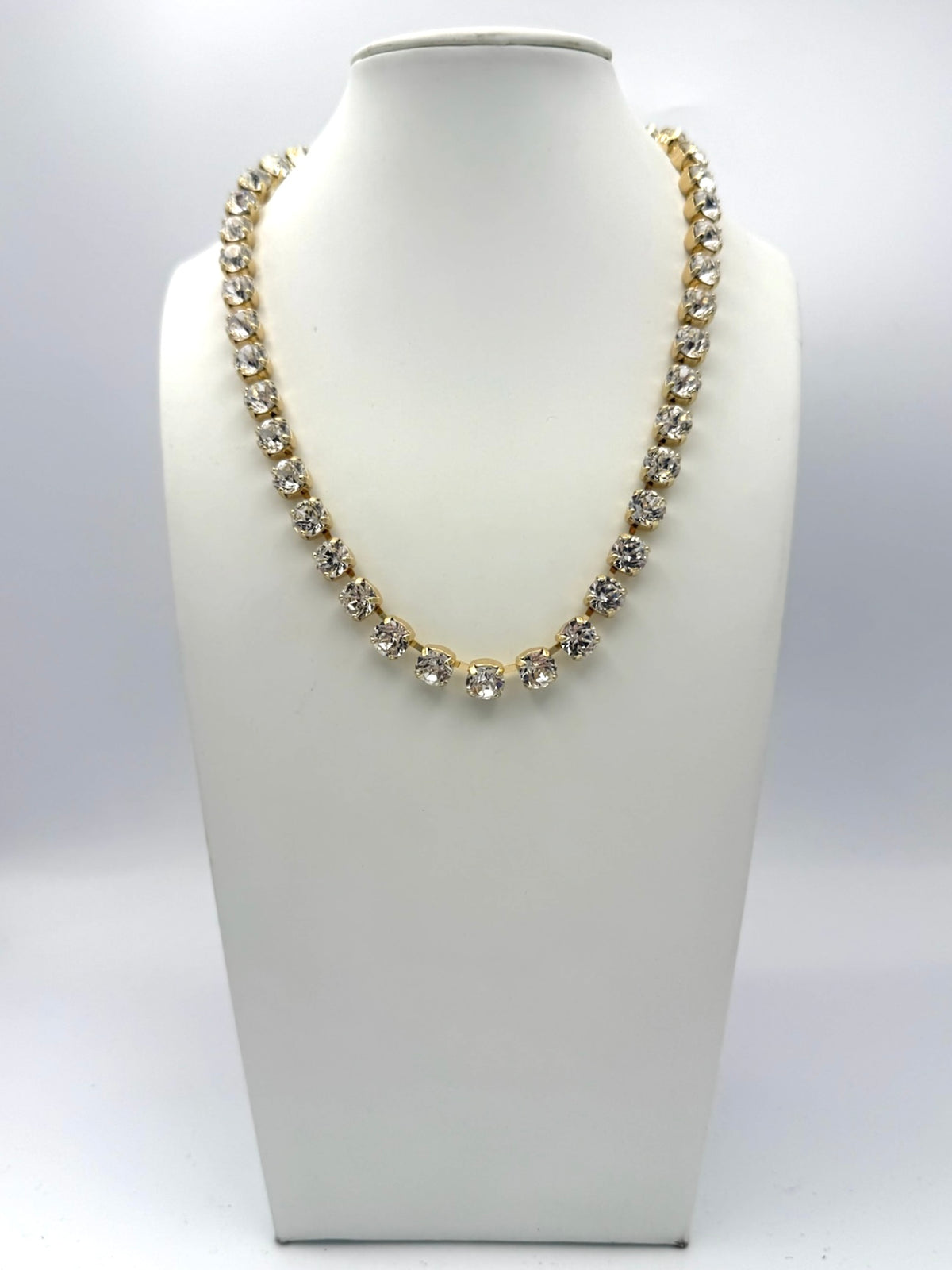 18-inch gold tennis necklace with clear round crystal rhinestones in prong settings on white jewelry bust.