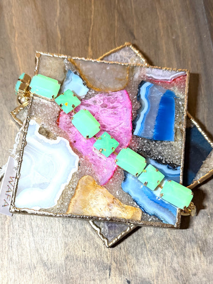 AF Designs jade green square gemstone tennis bracelet with gold prong settings displayed on colorful agate tray