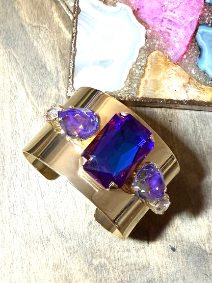 Wide gold cuff bracelet with large violet-blue emerald-cut center stone and lavender pear crystal accents