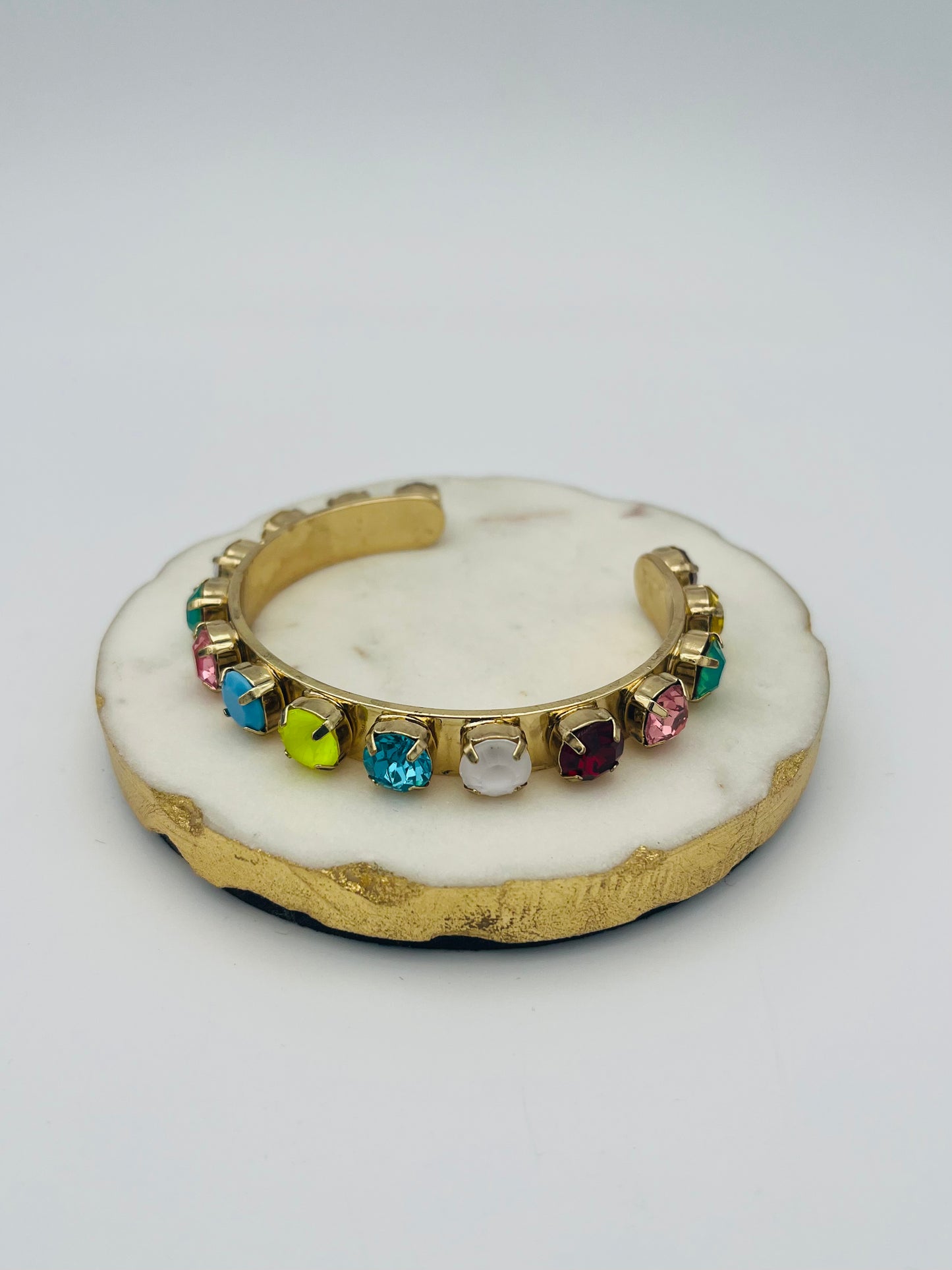 Gold cuff bracelet with colorful rainbow gemstones displayed on white marble dish