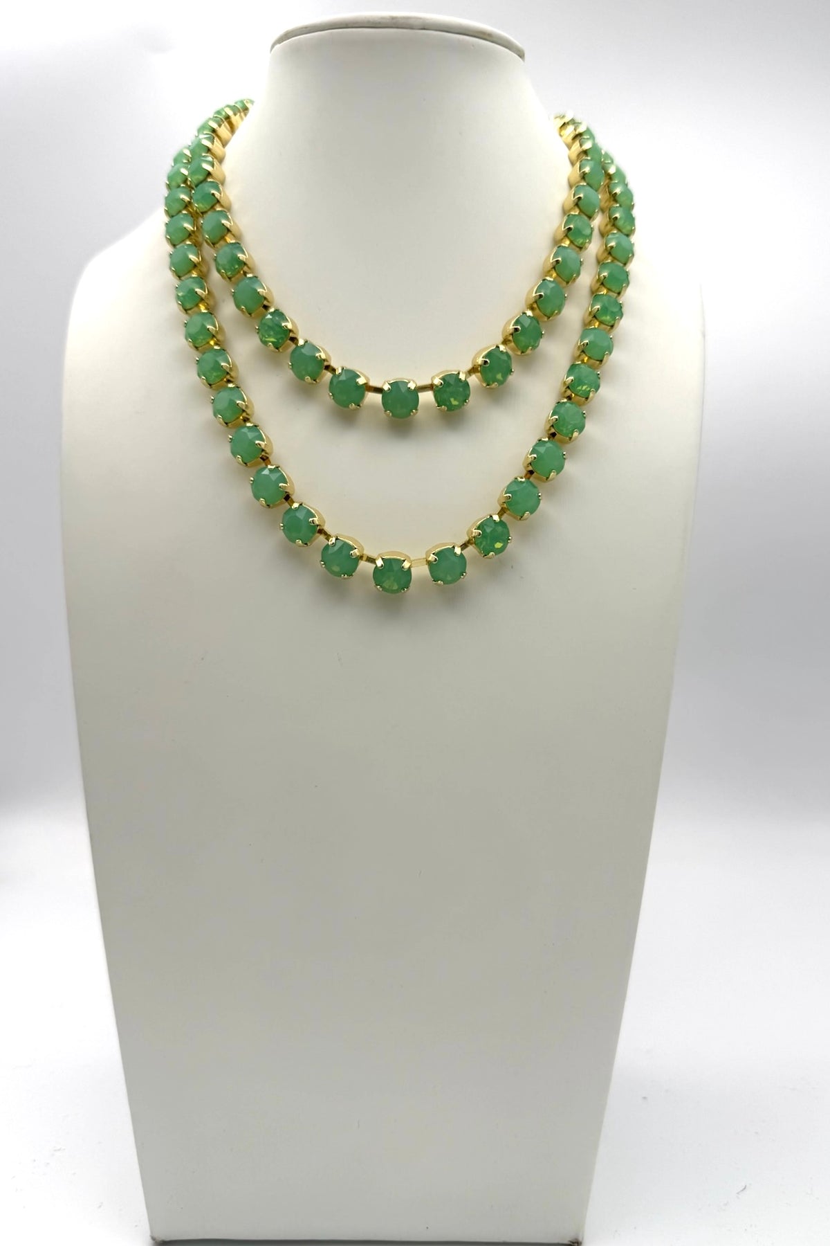 Double-strand jade green crystal tennis necklace with gold prong settings displayed on white jewelry bust