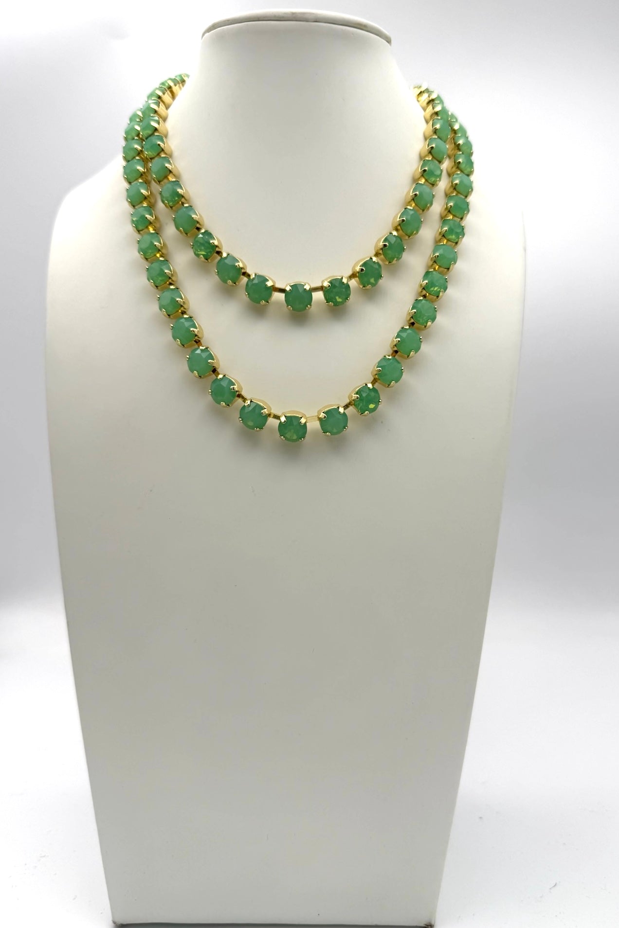 Double-strand jade green crystal tennis necklace with gold prong settings displayed on white jewelry bust