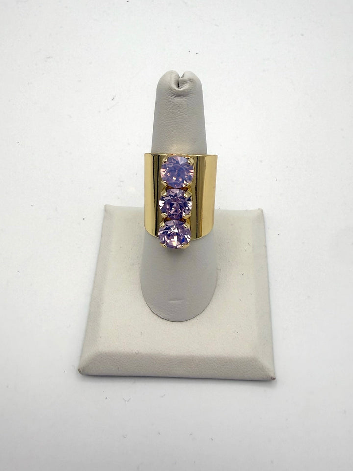 Triple Threat Ring in Lilac: wide gold band with three vertical round-cut lavender gemstones in prong settings.