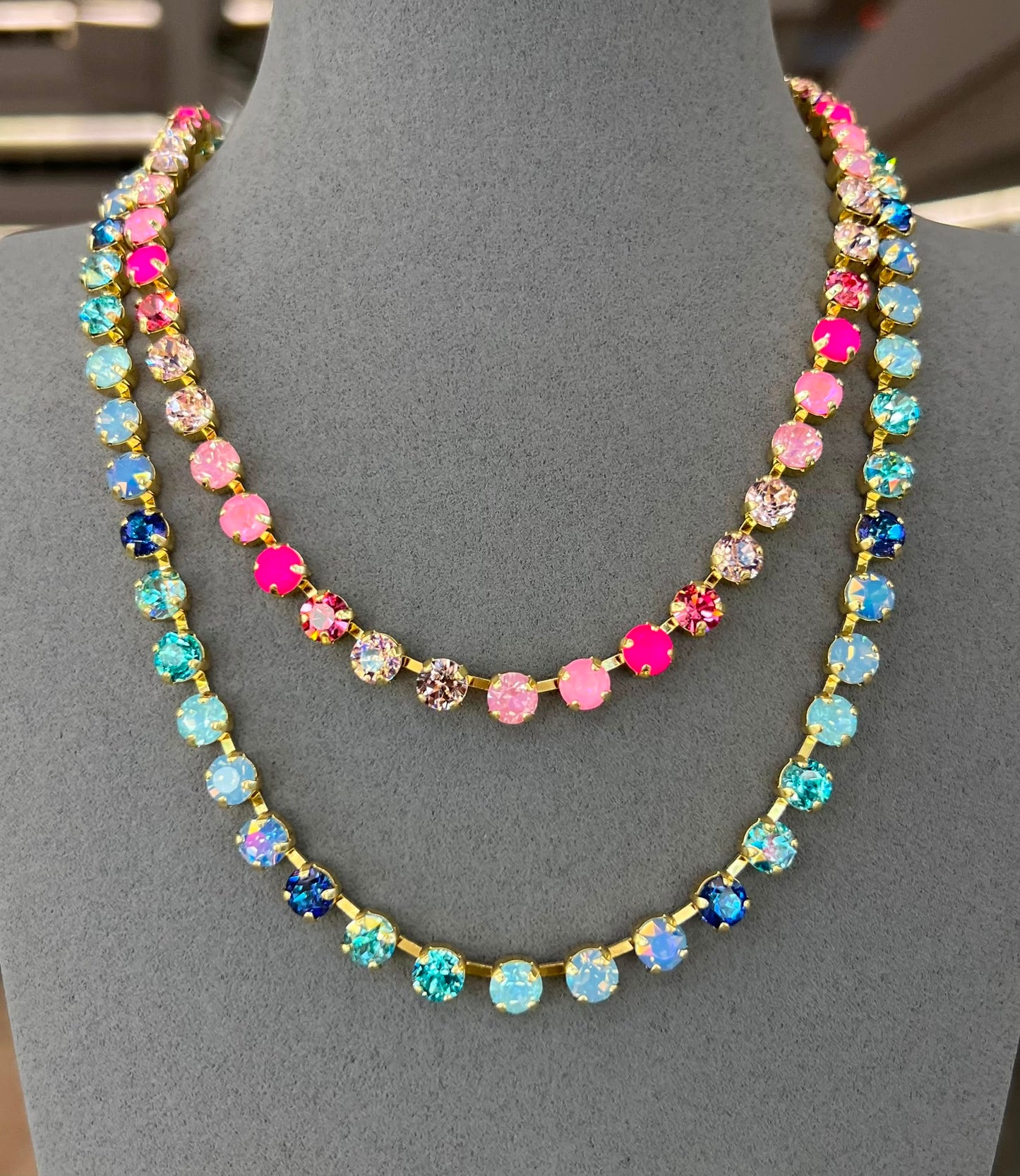 Two colorful rhinestone tennis necklaces layered on jewelry display - one pink/clear, one blue tones
