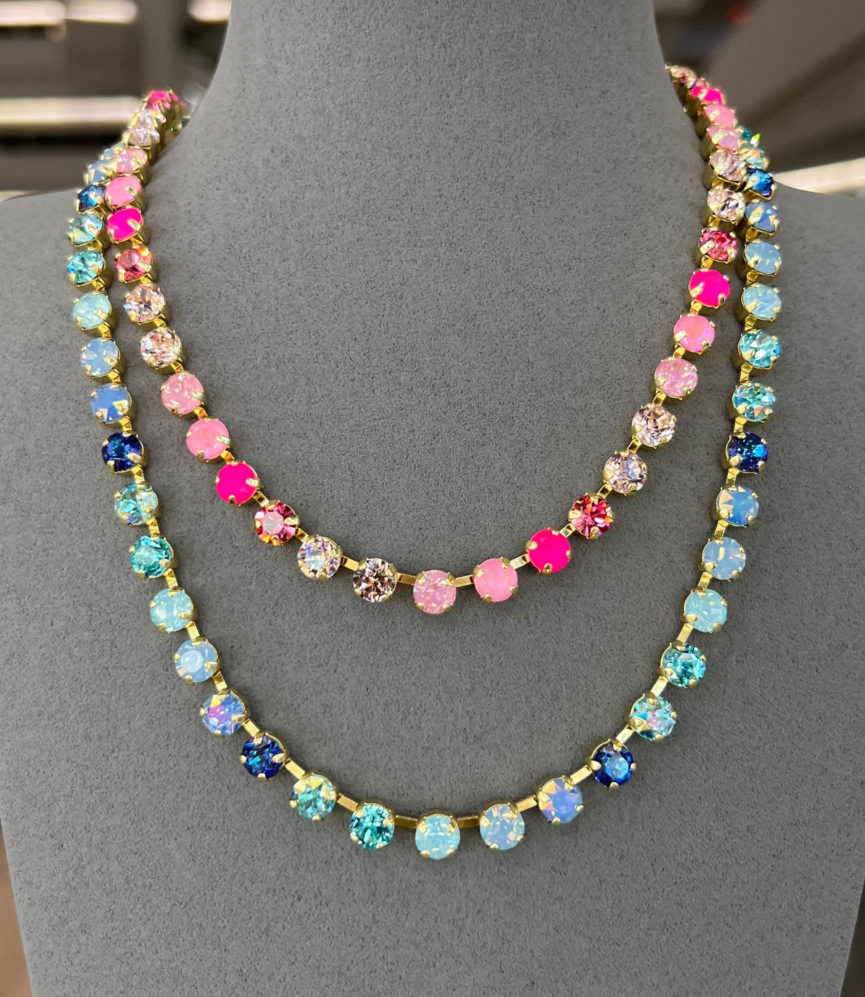 Two colorful rhinestone tennis necklaces layered on jewelry display - one pink/clear, one blue tones