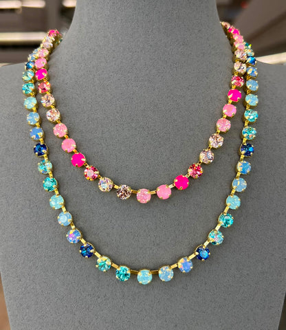 Two colorful rhinestone tennis necklaces layered on jewelry display - one pink/clear, one blue tones
