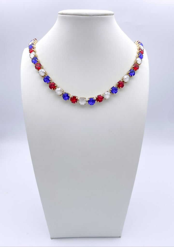 Red, white and blue gemstone tennis necklace in gold setting displayed on white jewelry bust