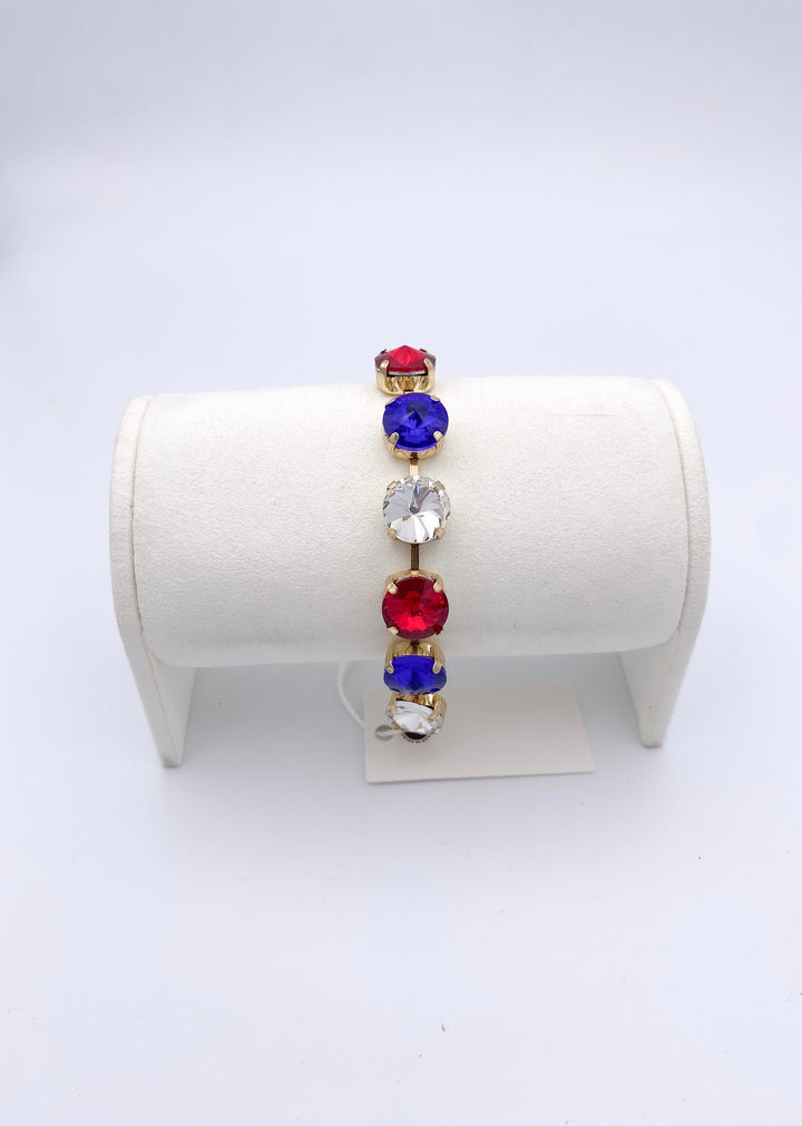 Sienna tennis bracelet with red, blue and clear oval gemstones in gold settings displayed on white jewelry stand