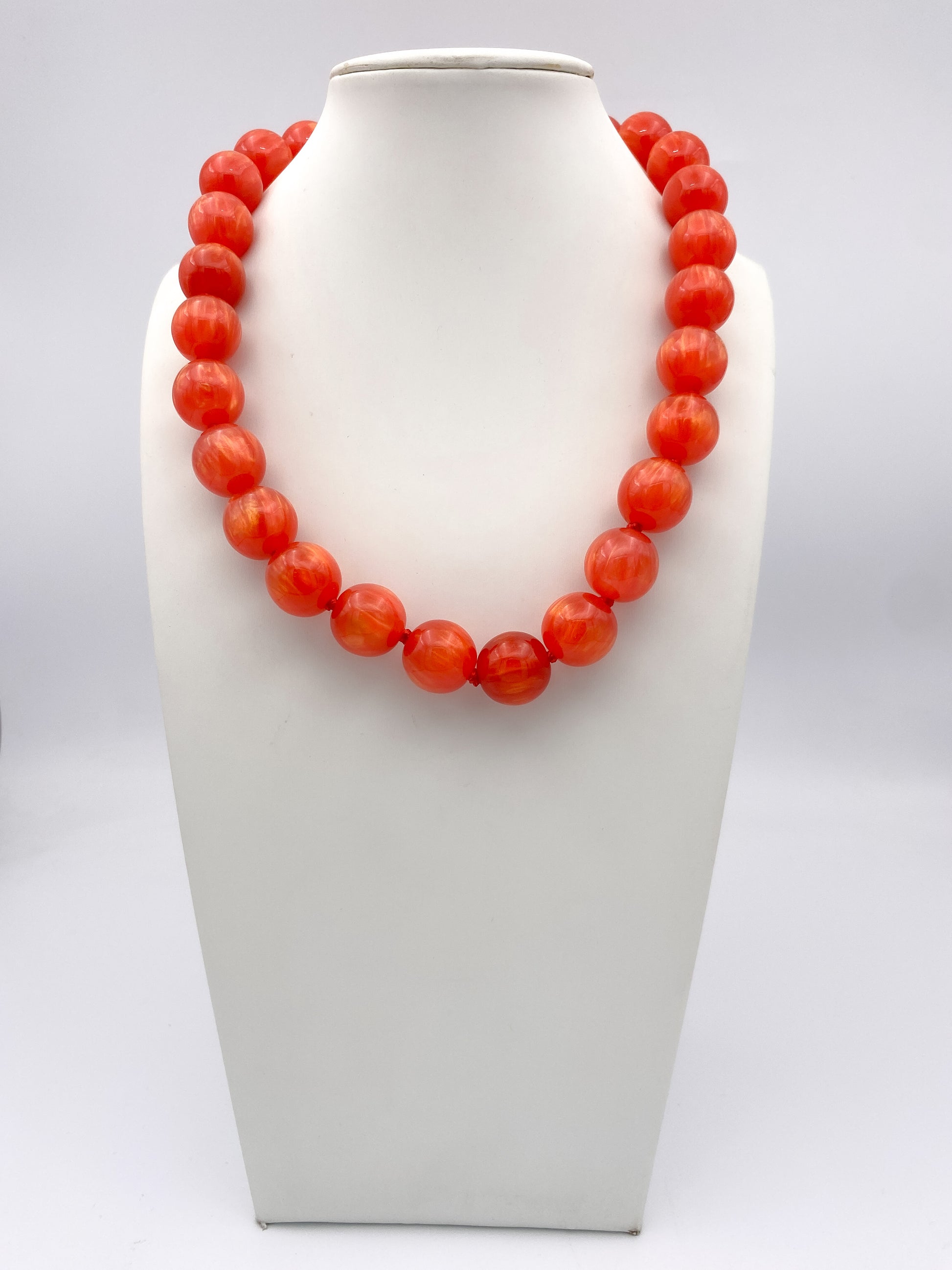 Bold coral orange marbled round bead statement necklace on white jewelry bust, single strand, knotted