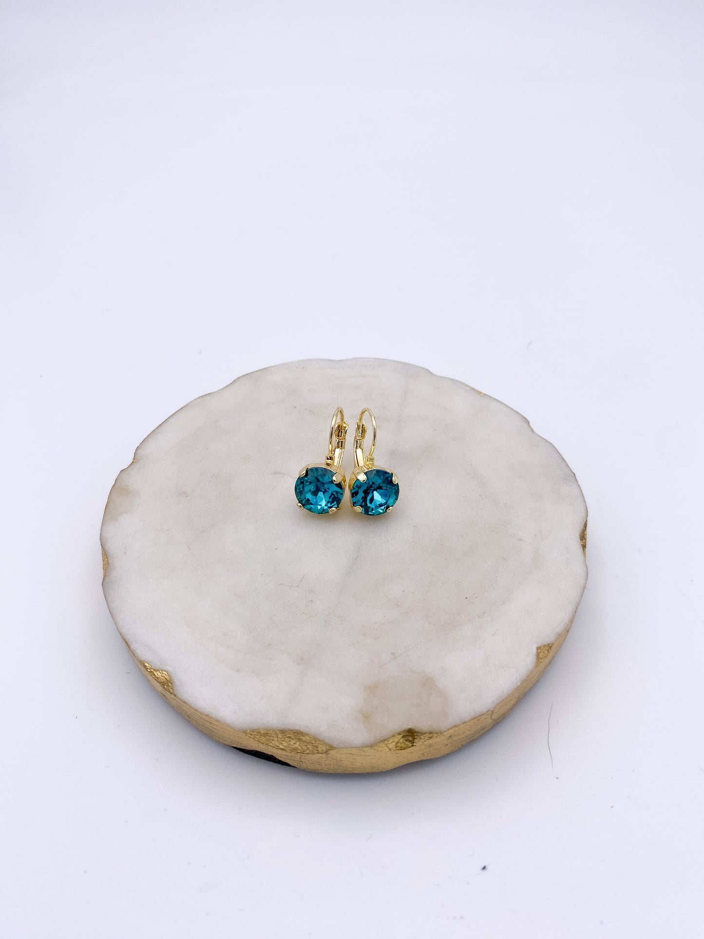 Gold lever-back drop earrings with round faceted teal ocean blue crystals, displayed on marble tray