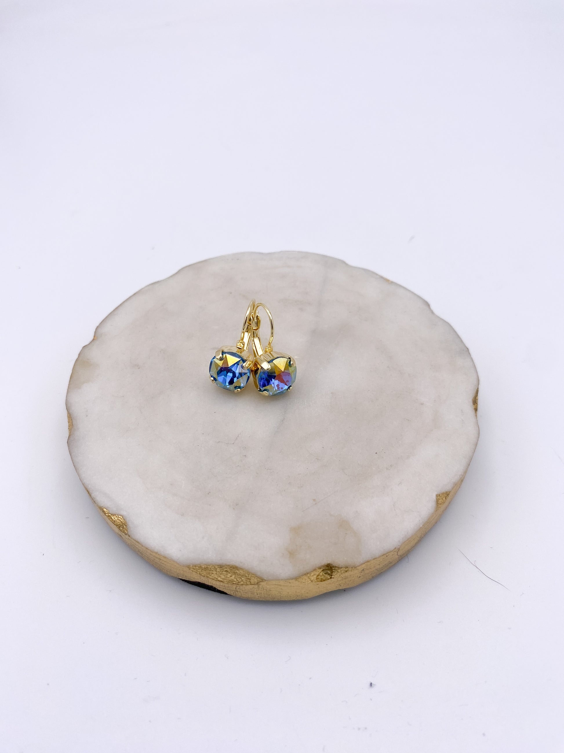 Gold lever-back drop earrings with iridescent blue AB faceted crystal stones on marble tray