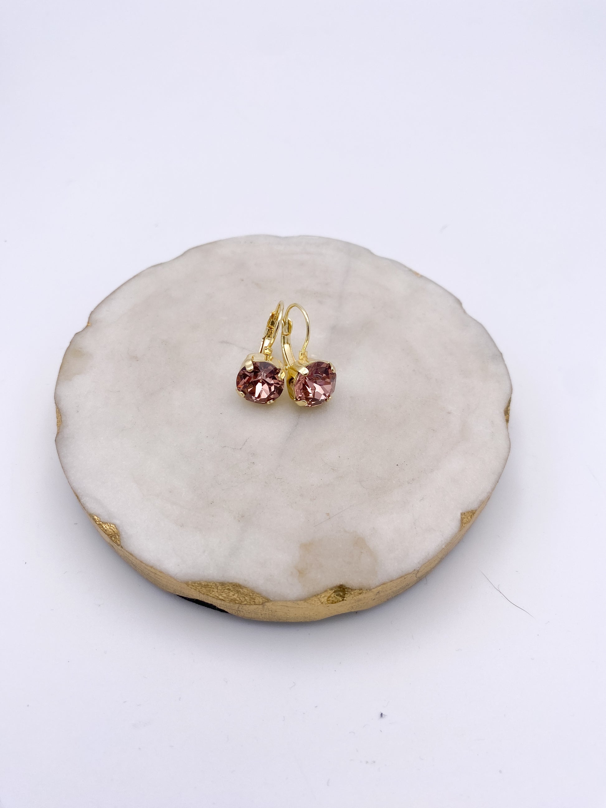 Gold lever-back drop earrings with round faceted blush pink peony crystals on white marble dish