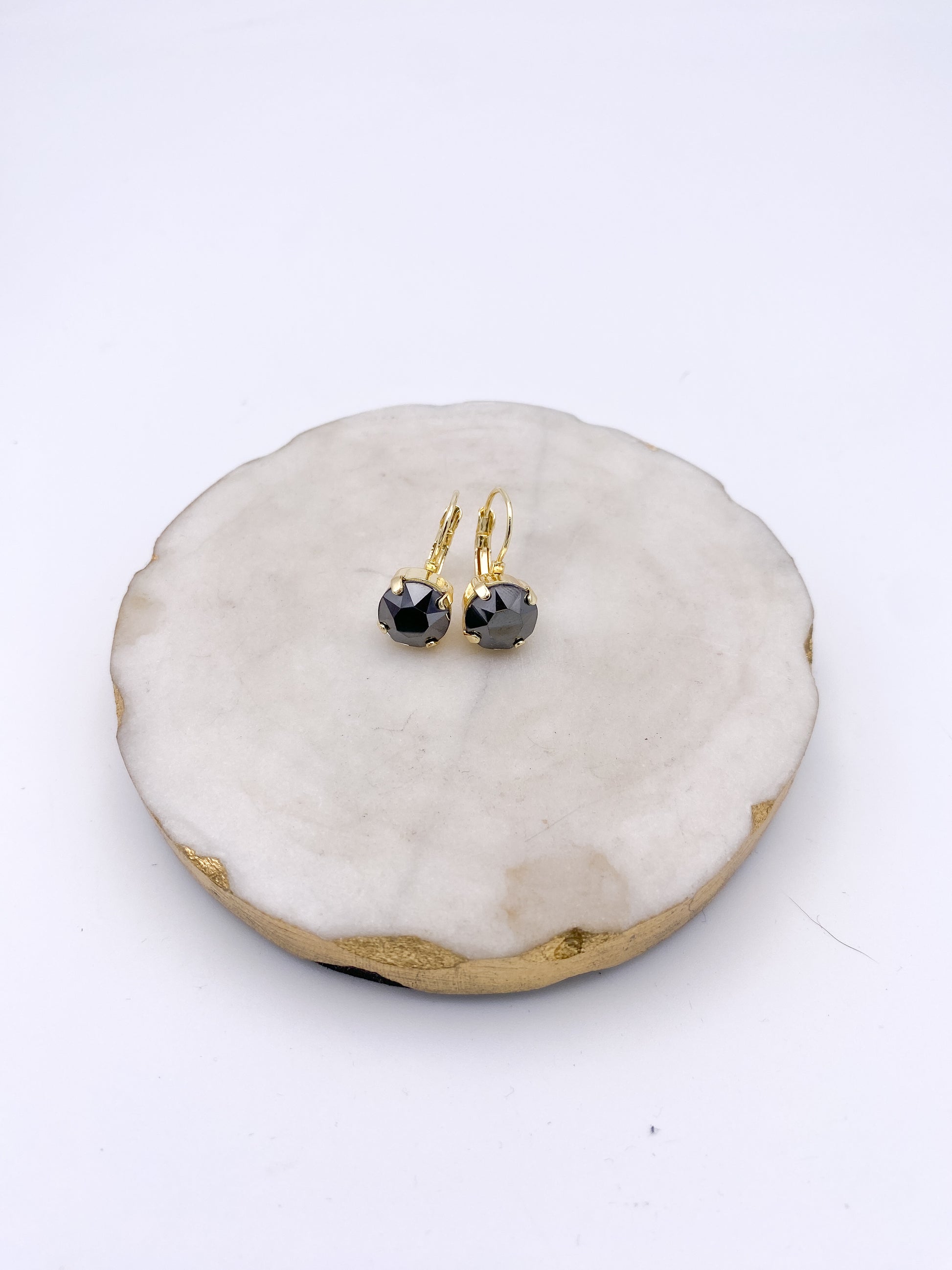 Gold lever-back drop earrings with round faceted black crystal stones, displayed on white marble tray.