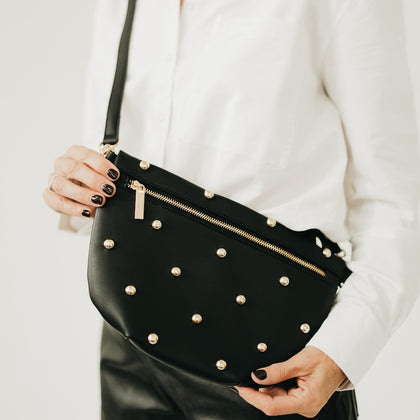 Black leather crossbody bum bag with gold dome studs and gold zipper, worn as a shoulder bag.